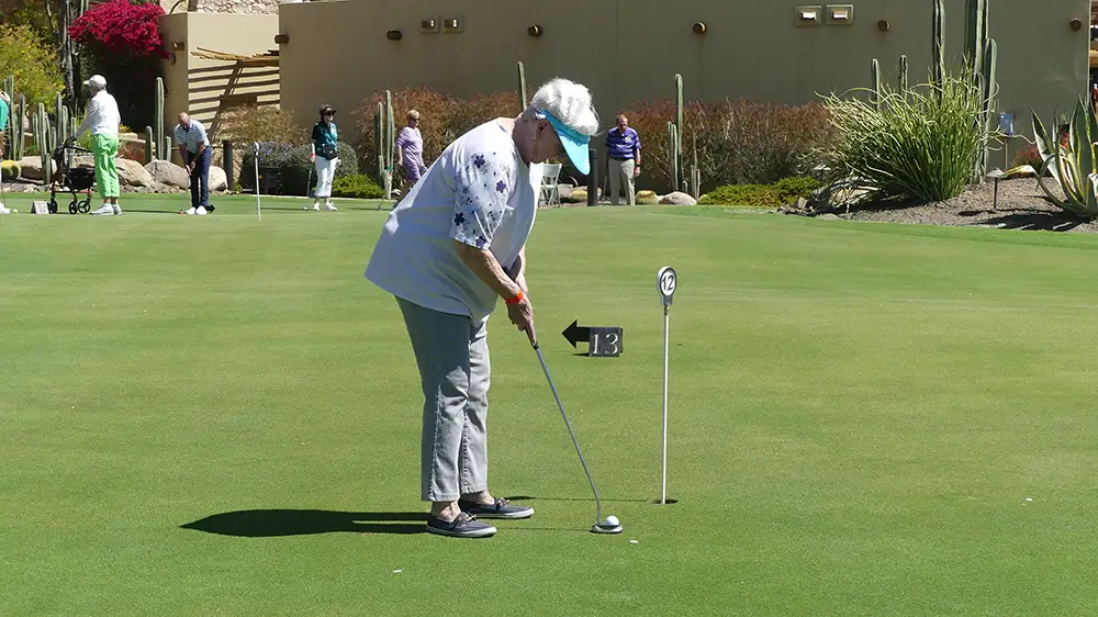 A senior woman wearing a visor lines up a putt on a lush green golf course, illustrating the active outdoor lifestyle available to seniors at Sagewood in luxury retirement communities.