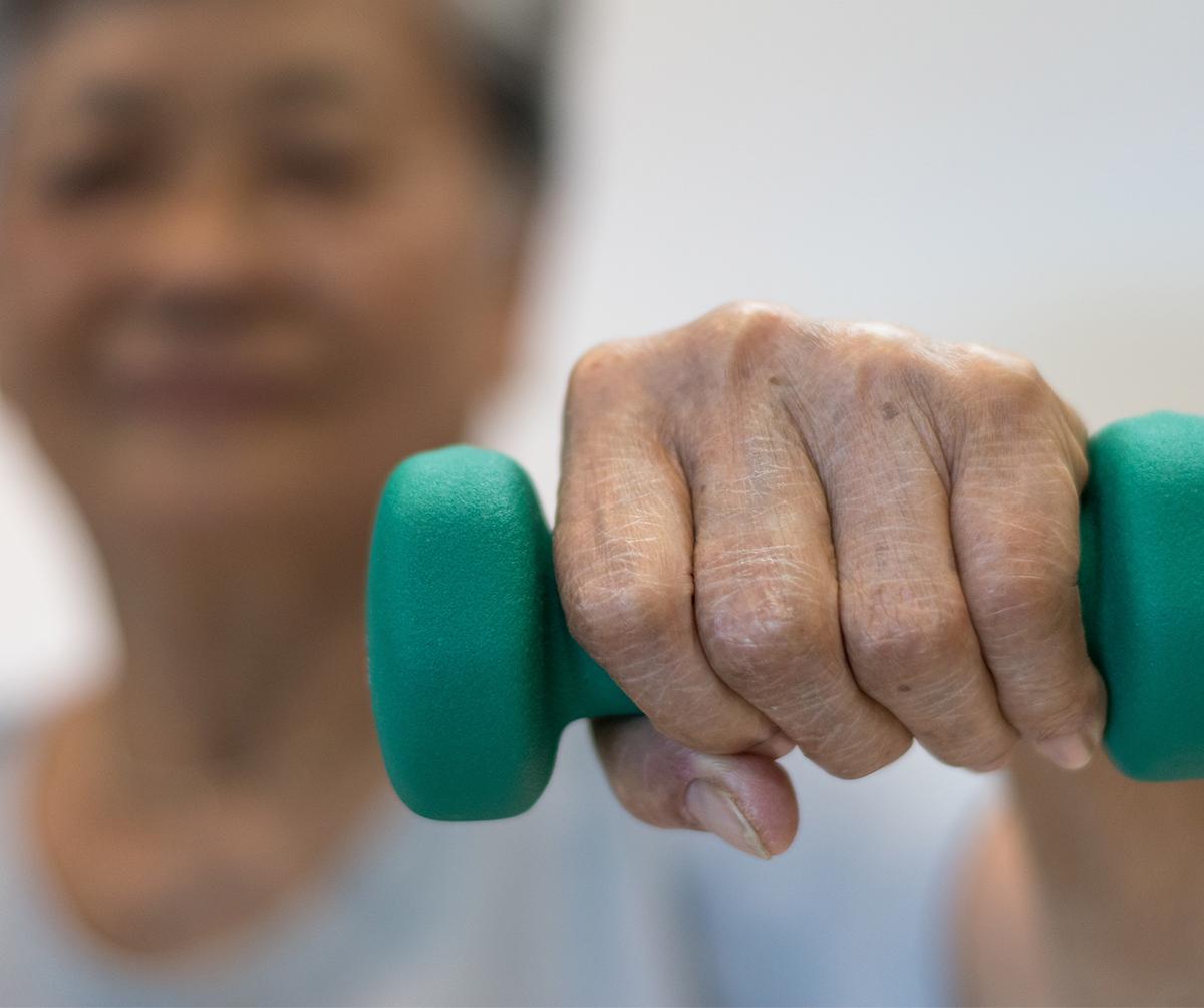 a senior woman lifting a light weight toward the camera for weight training