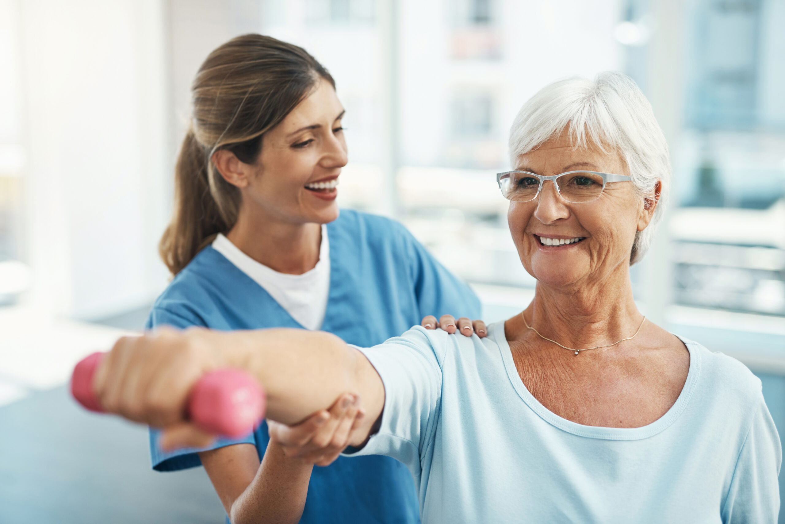 Senior woman, doctor and helping in weightlifting for physical exercise or activity at the hospital. Happy nurse, therapist or physician assisting elderly lady in workout or training at the clinic
